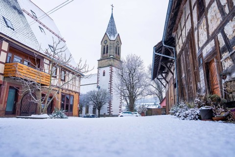 A snowy church tower next to half-timbered houses in a quiet village, Gechingen, Calw district,