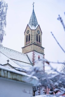 Snowy church tower with gothic elements and surrounding trees in winter, Gechingen, Calw district,