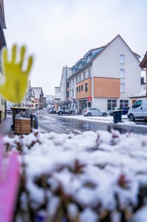 Snowy city street with residential buildings in the background and parked cars, Gechingen, Calw