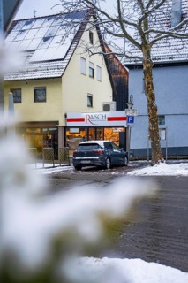 Snowy city street with parked car in front of a building with a shop, Gechingen, Calw district,
