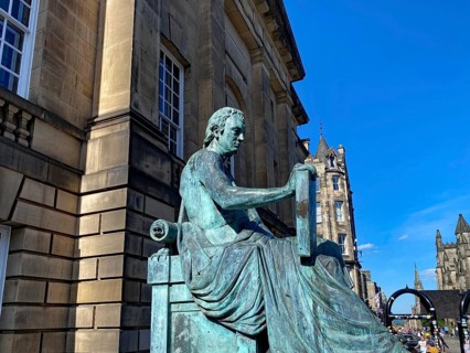 Bronze statue of a man sitting in front of a historic building under a clear sky