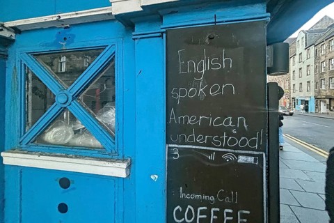 A blue-painted kiosk with a sign advertising English language skills, Humor, Royal Mile, Edinburgh,