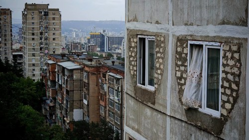 Old apartment blocks with worn facades against a city backdrop, nostalgic curtain blowing out the
