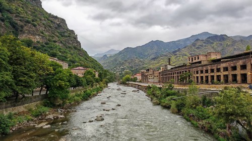 A river flows through a valley surrounded by mountains and old factory buildings, Armenia