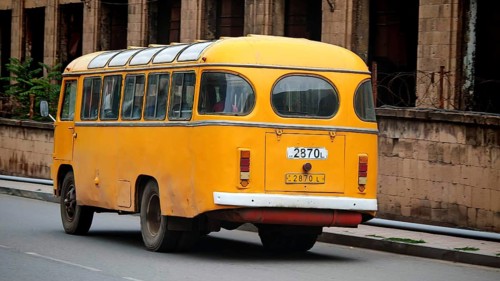 A yellow retro bus passes an old brick building along the road, Armenia