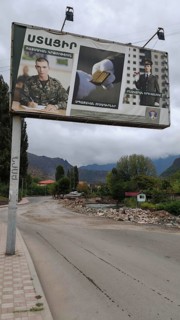 A large advertising poster on the side of the road, army looking for soldiers with mountains in the