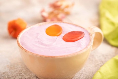 Purple Yogurt, with jelly candy on brown concrete background and green textile, side view, close