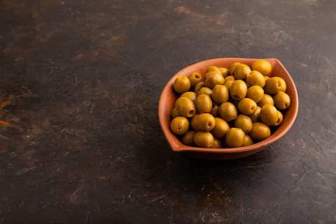 Fresh green olives in ceramic clay bowl on black concrete background. side view, copy space
