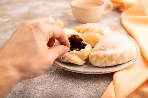 Glazed Pies with blueberry jam on brown concrete background and orange linen textile with hand, cup