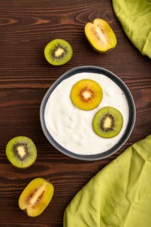Yogurt, with kiwi in blue bowl on brown wooden background and green linen textile, top view, flat