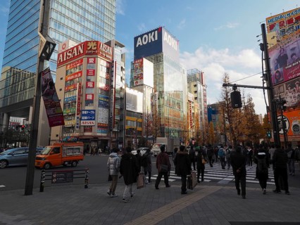 People cross a busy city street surrounded by modern buildings and commercials, Akihabara Electric