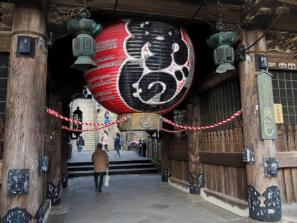 A large temple with an impressive lantern and traditional wooden construction, people enter the