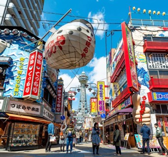 Lots of colorful signs in a pedestrian zone with shops and restaurants, behind Tsutenkaku Tower,