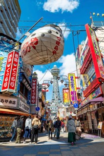 Lots of colorful signs in a pedestrian zone with shops and restaurants, behind Tsutenkaku Tower,