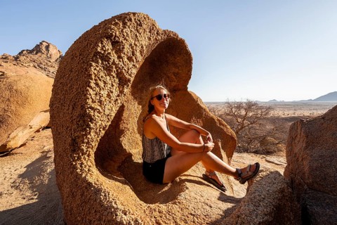 Woman sitting quietly in a rock in the sunny desert landscape, Spitzkoppe, Namibia