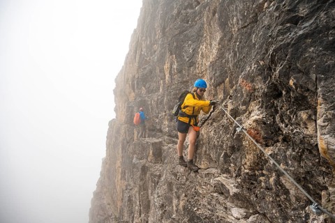 Mountaineers on a ladder on the Via Ferrata Oliva Detassis via ferrata in fog, rocky mountain peaks