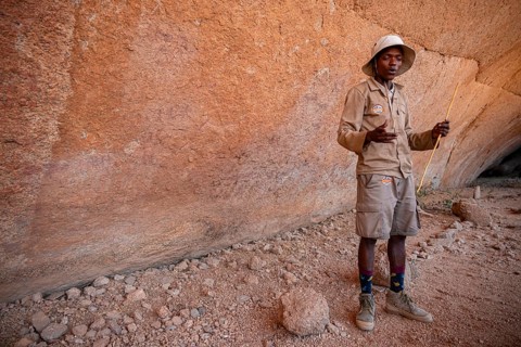 Bushman's paradise, guide standing in front of a massive red rock wall in a desert-like