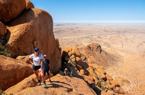 Tourists hiking on a rock with a view of a vast desert landscape, Spitzkoppe, Namibia