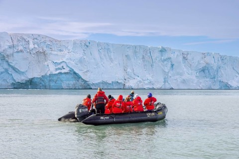 Eco-tourists in Zodiac boat from Poseidon Expeditions looking at Brasvellbreen glacier wall