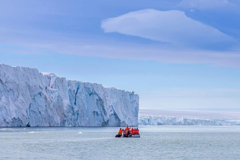 Eco-tourists in Zodiac boat and Brasvellbreen glacier wall from ice cap Austfonna debouching into