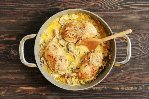 Top view of homemade creamy chicken thighs with mushroom sauce in skillet, served with herbs on