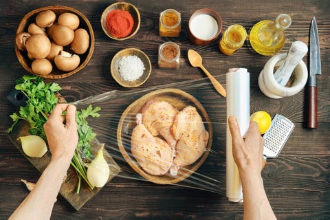 Hands wrapping marinated chicken with plastic stretch film for marinating. High angle view of