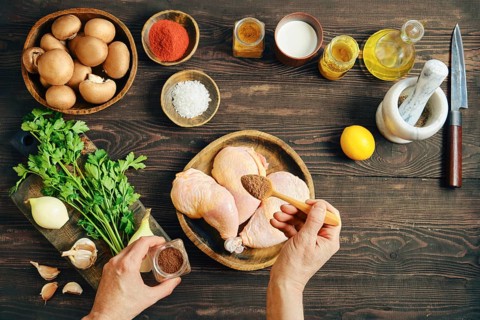 Top view of hands seasoning raw chicken legs with spicy pepper mix while preparing food on dark
