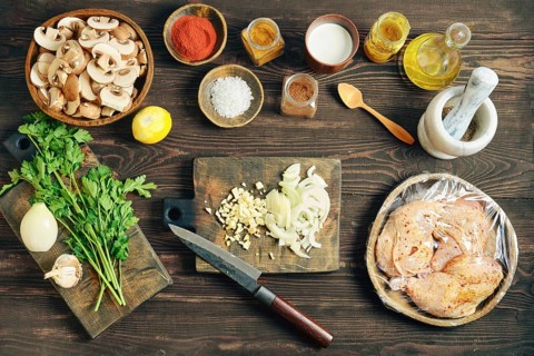 Top view of lifestyle food prep with sliced mushroom and wrapped chicken on a dark rustic wooden
