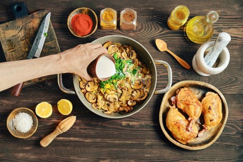 Pouring heavy cream to a pot filled with fried onion and mushrooms. Process of preparing creamy