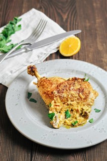A chicken leg is placed on a gray plate. It is golden brown and garnished with green herbs. A piece