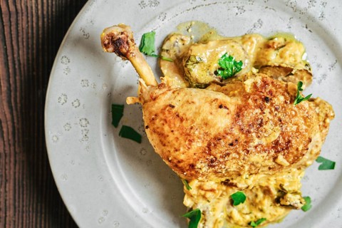 Close-up top view of roasted chicken leg on a round plate with a creamy mushroom sauce and herbs