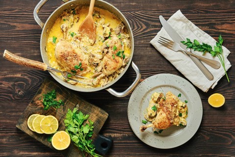 Top view of home-cooked creamy chicken legs in mushroom sauce served with parsley and lemon on