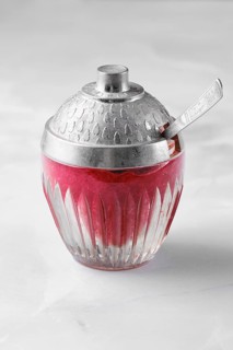 A bowl made of glass with a silver lid is filled with red lingonberry jam or sauce and sits on a