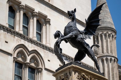 Metal statue of a winged dragon in front of the neo-Gothic building of the Royal Court of Justice,