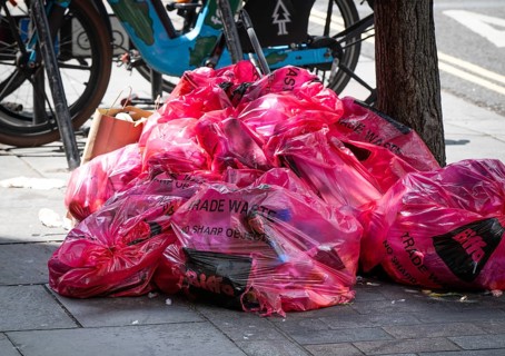 A pile of pink plastic bags with the words Trade Waste lying on the side of the road on the