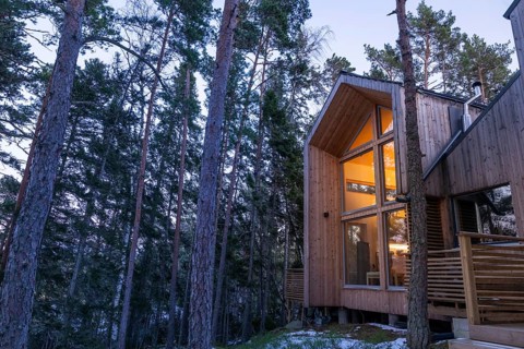 Modern wooden house in the forest, illuminated from within and inviting at dusk, Korpoström, Korpo