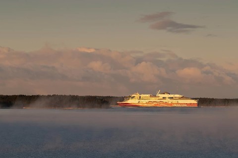 Large Viking Line ferry sails on the calm sea near a wooded shore at sunrise, Korpoström, Korpo or
