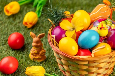 Colourful Easter eggs in a basket with a rabbit figure and flowers on grass