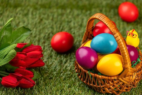 A basket of colorful Easter eggs next to flowers in a meadow