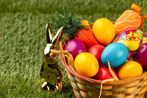 Colourful Easter eggs and a golden rabbit figure next to a basket on grass