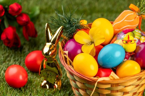A basket with colorful Easter eggs and a rabbit statue on grass