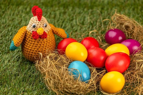 Crocheted chicken and colorful easter eggs in a nest on grass