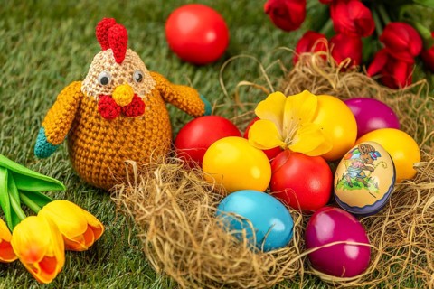 Crocheted chicken and colorful easter eggs with tulips on green grass