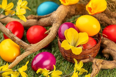Colourful Easter eggs in and around a small basket, branches and blossoms on grass