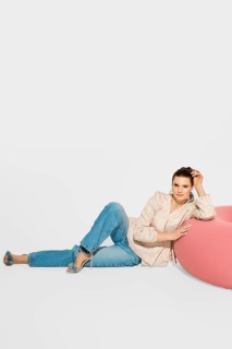 A woman is lying near a pink bean bag, leaning her torso back while resting on her left arm. She