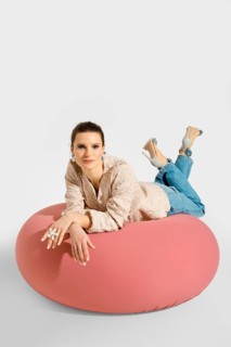 A woman lies on a pink bean bag with her legs raised and feet resting on the cushion. She wears a