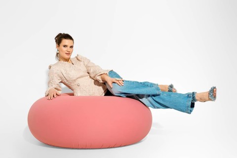 Woman is lying on a large pink lounge chair with casual clothes. The setting is a studio with