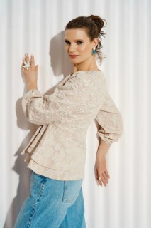 A woman leaning to the wall. She wears a light-colored outfit and shows a playful expression. The