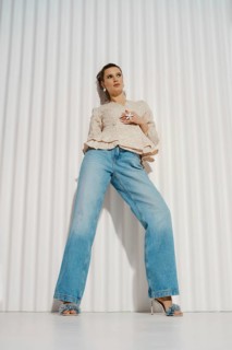 A woman stands confidently in a relaxed pose wearing wide-leg jeans and a light blouse. She is in a