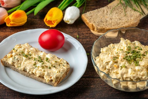 Egg salad on a plate with bread, surrounded by fresh ingredients and flowers